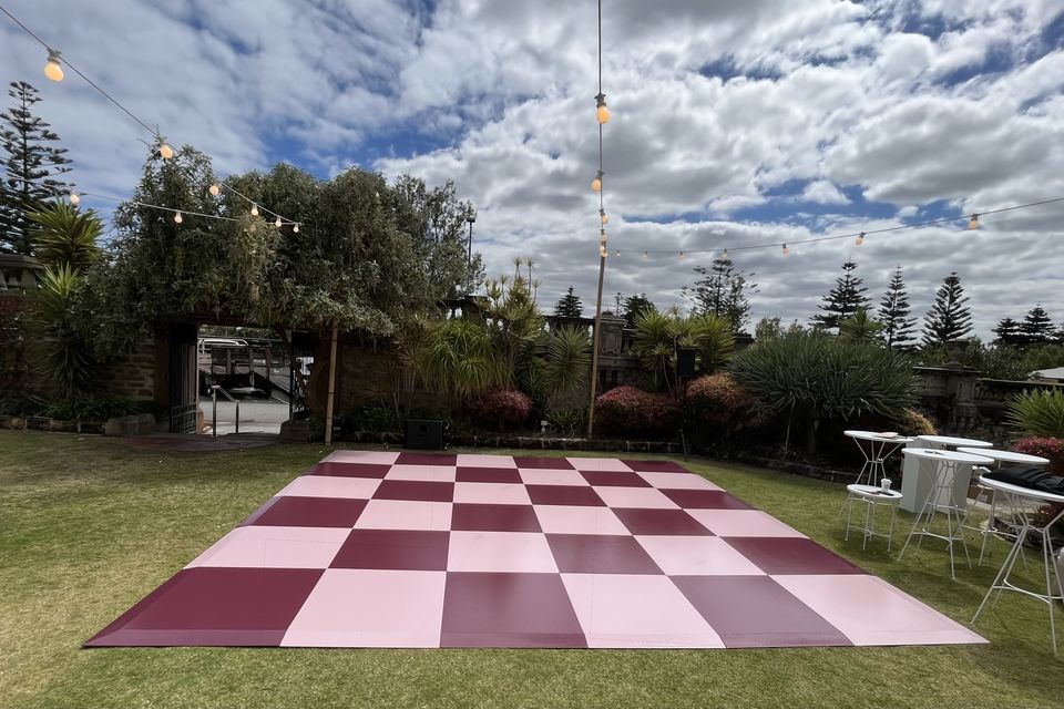 Pink and maroon checkered dance floor on a lawn under festoon lights