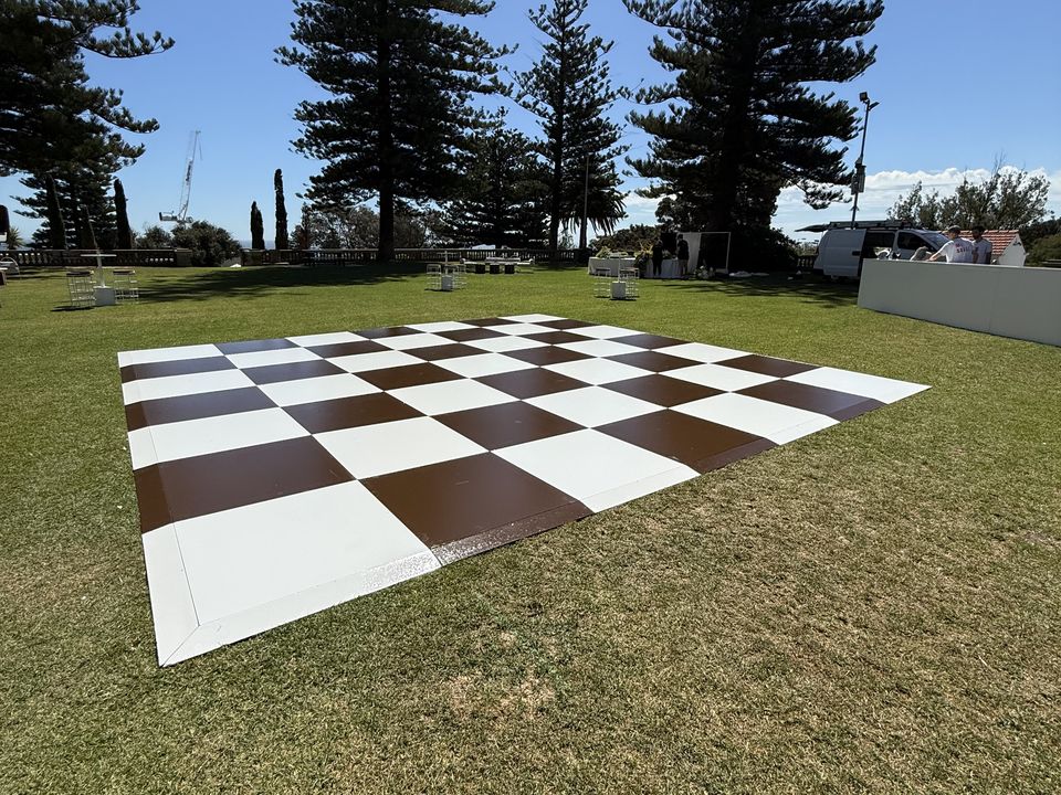 Brown and white checkered dance floor on a lawn under tall Norfolk Island pines