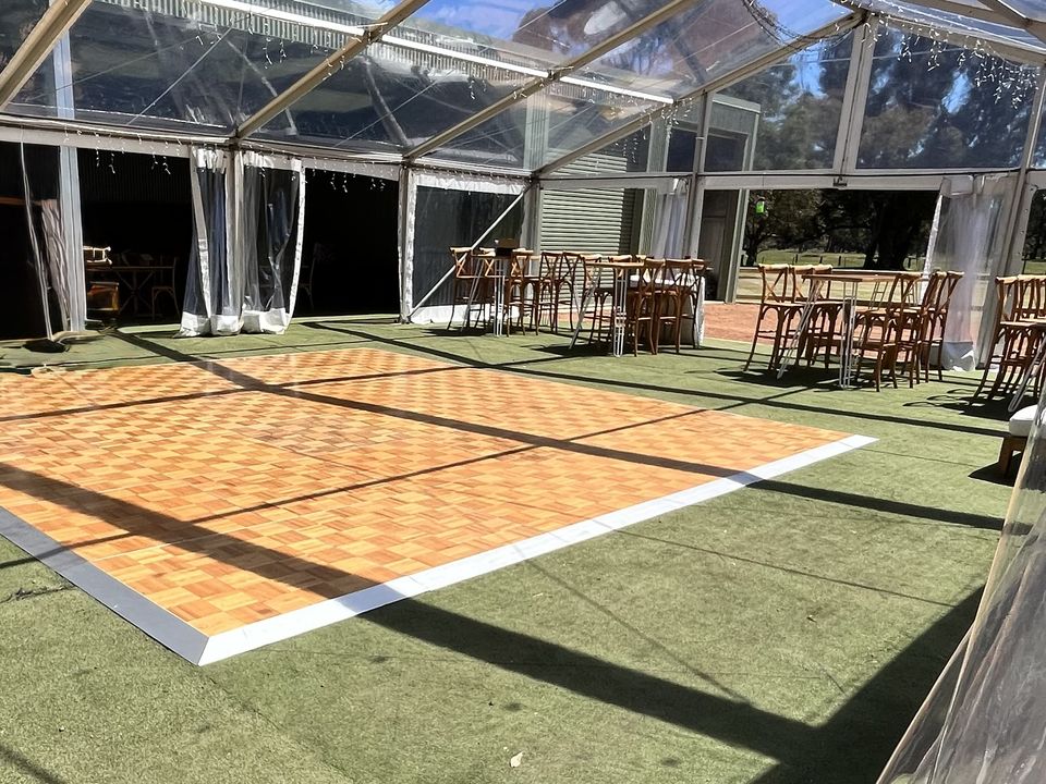 Parquetry dance floor with white edging inside a clear-roof marquee