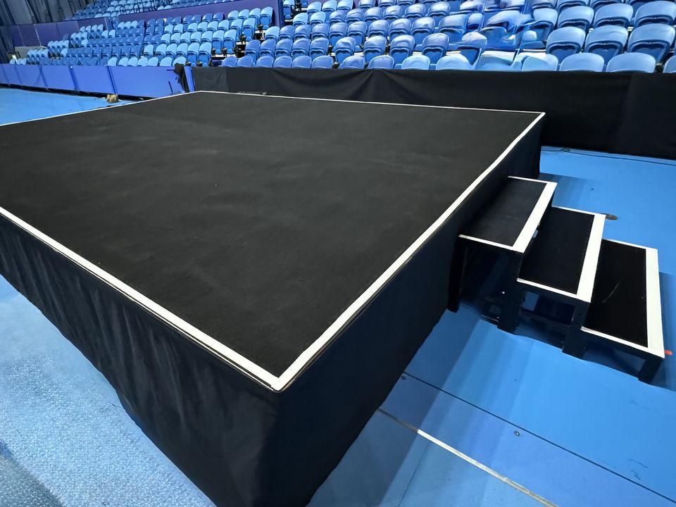 Black carpeted stage with white edge trim and a three-step unit in an indoor arena