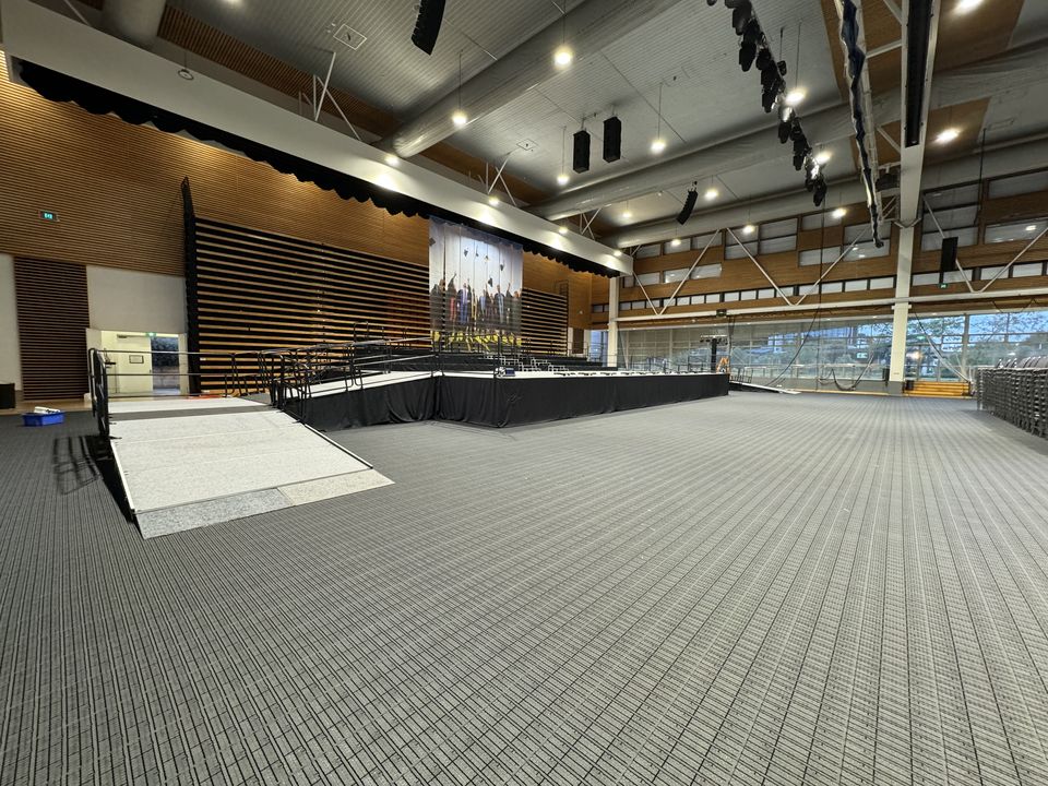 Long access ramp with handrails rising to a stage in a large hall