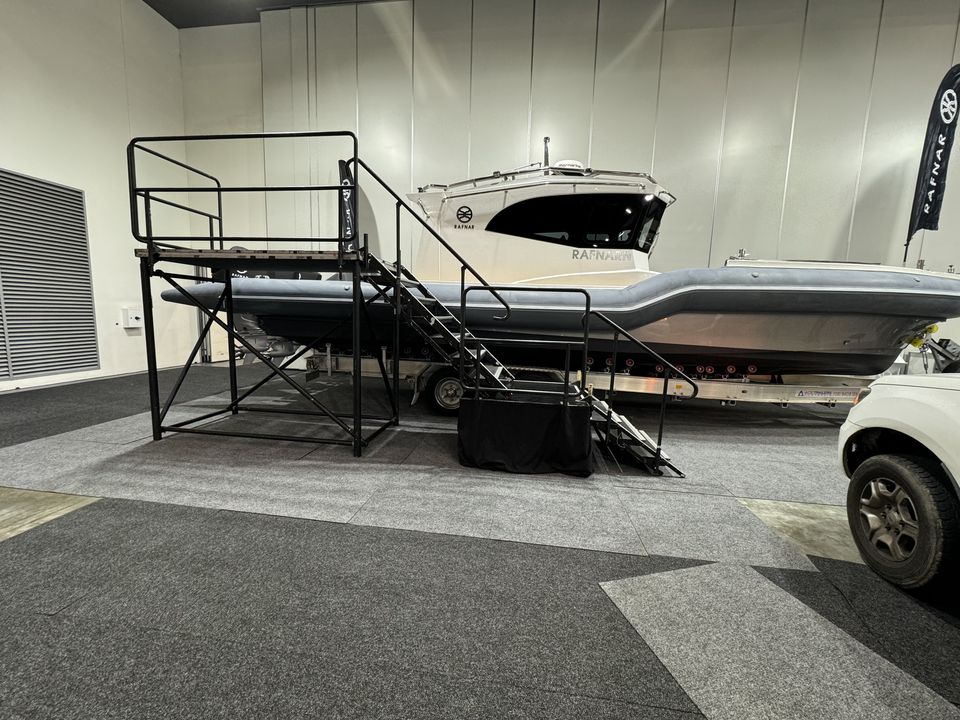 Black viewing platform with stairs and handrails beside a boat on display