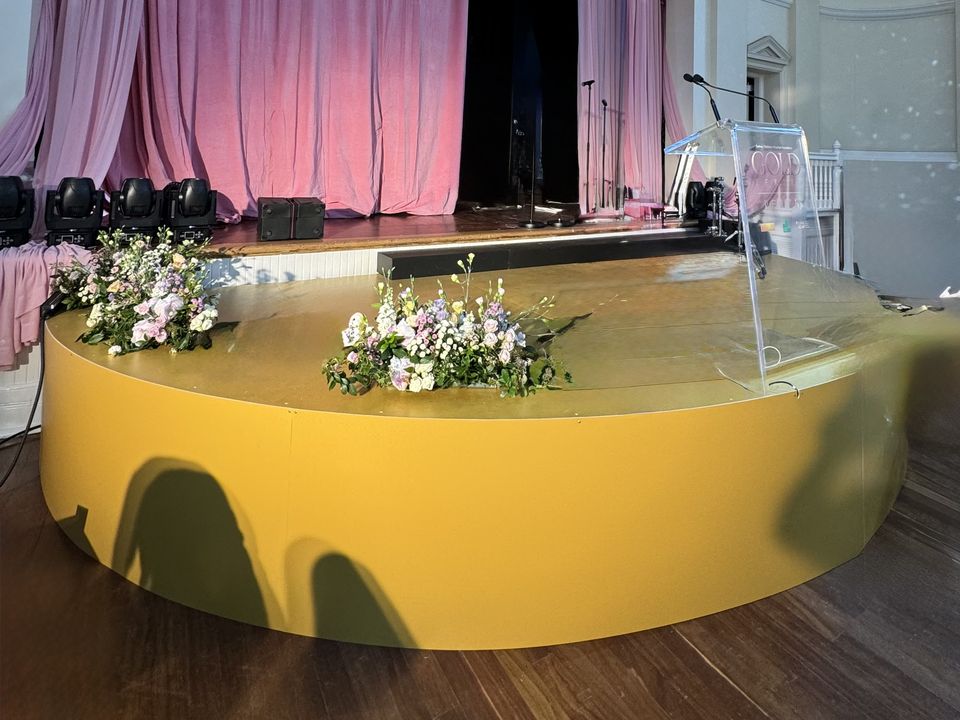 Curved yellow-fronted stage with flowers in front of a draped proscenium stage