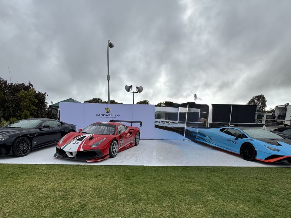 Low white display platform on a lawn with four sports cars