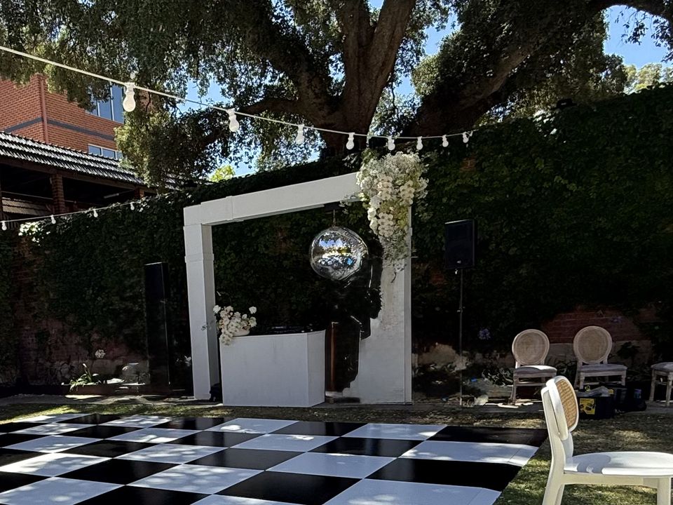 Mirror ball hanging in a white arch over a black and white dance floor, with festoon lights strung above
