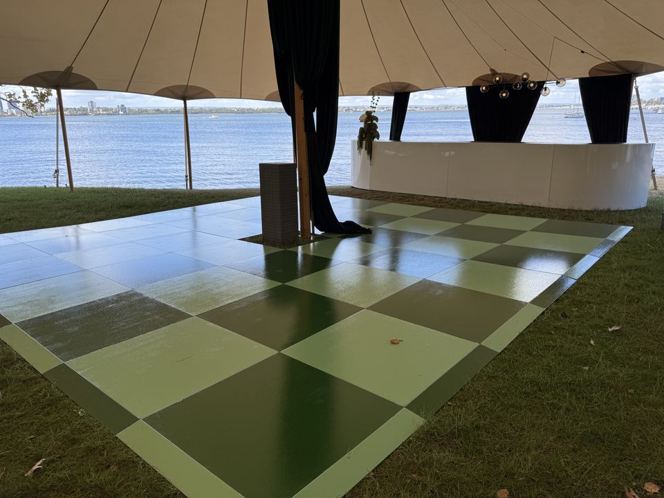 Green checkered dance floor on grass under a sailcloth tent beside the river
