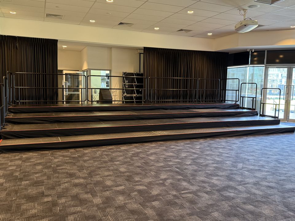 Four-tier black risers with handrails along a carpeted function room