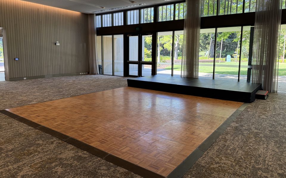Parquetry dance floor with black edging in a function room with floor-to-ceiling windows and a stage behind
