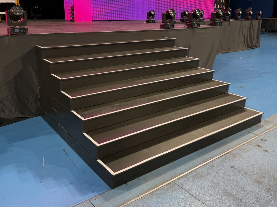 Wide black stage steps with LED edge lighting leading up to a stage with a pink LED wall
